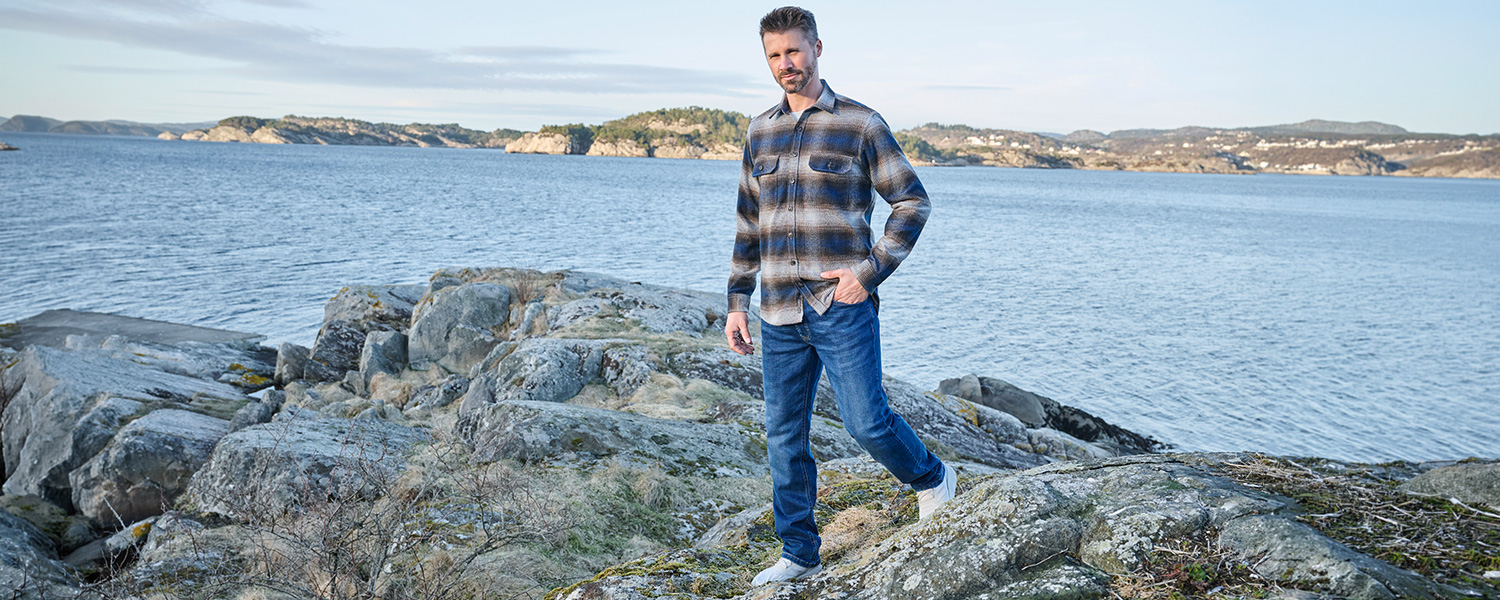 Mann in kariertem Braun-Blauem Freizeithemd aus Wolle, kombiniert mit Jeans am Meer