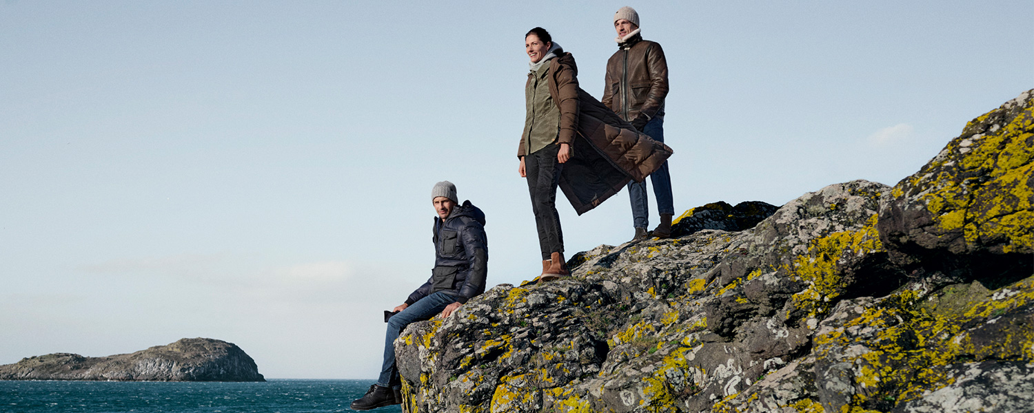 Grüne Winterjacke mit Kapuze, lässig getragen auf Steinklippen am Meer