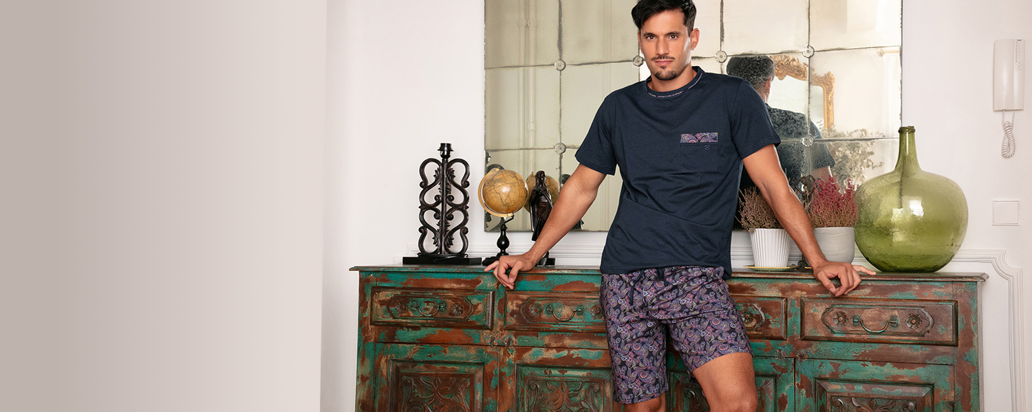 Mann in dunkelblauem T-Shirt und gemusterten Shorts, lässig an Kommode gelehnt