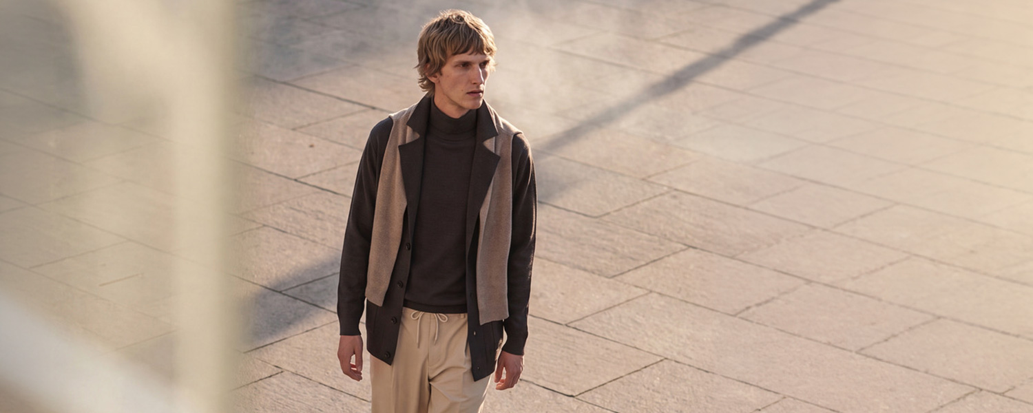 Mann in braunem Rollkragenpullover und Sakko, beige Hose, draußen bei Tageslicht