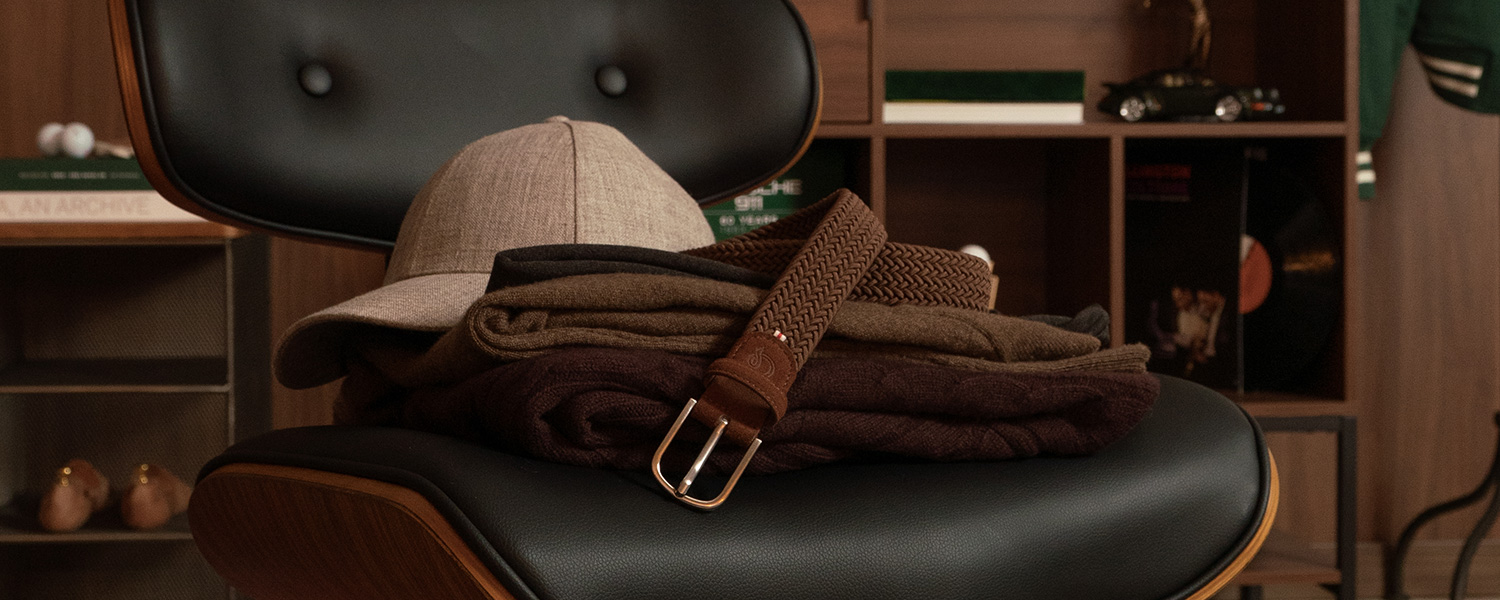 Herren-Kaschmirpullover in Braun, beige Kappe und geflochtener Gürtel auf einem Stuhl drapiert
