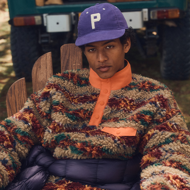 Mann in bunt gemustertem Fleecepullover mit orangefarbenem Detail, leger im Freien sitzend