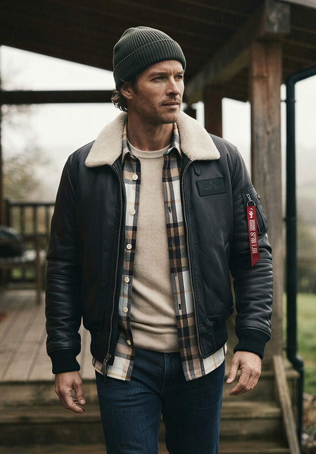 Herr in schwarzer Fliegerjacke mit Fellkragen, kariertes Hemd, Jeans, draußen stehend