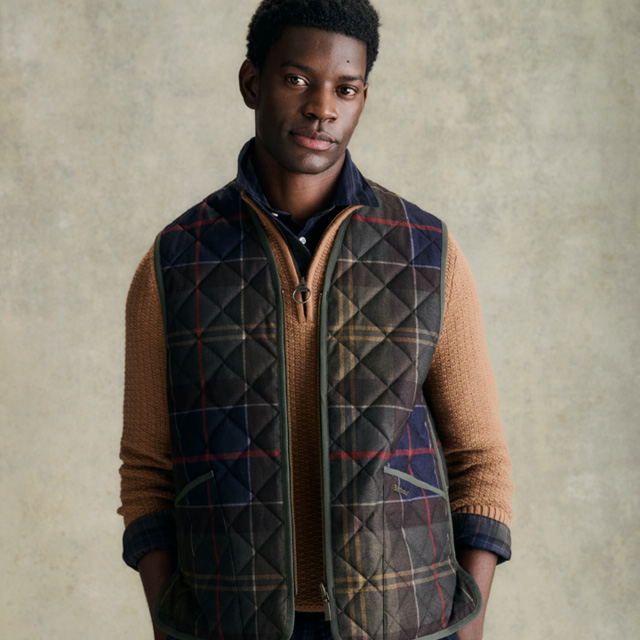 Mann in karierter, gesteppter Weste über beigem Strickpullover, casual getragen
