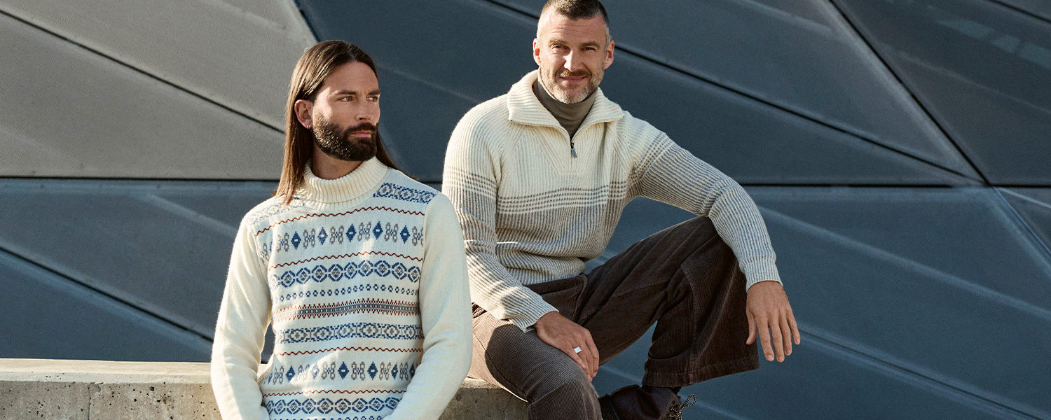 Herren in cremefarbenem Strickpullover mit Muster und grauem Troyer-Pullover, lässig im Freien getragen