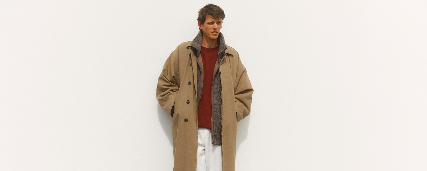 Eleganter beiger Mantel mit Knopfleiste, getragen über rotem Pullover und weißer Hose
