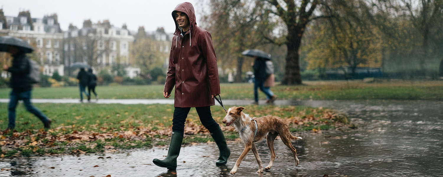 Mann in bordeauxfarbener Regenjacke mit Kapuze und schwarzer Hose beim Spaziergang im Park