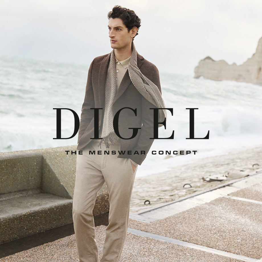 Mann in braunem Strickpullover mit gestreiftem Schal und beiger Chino-Hose am Meer