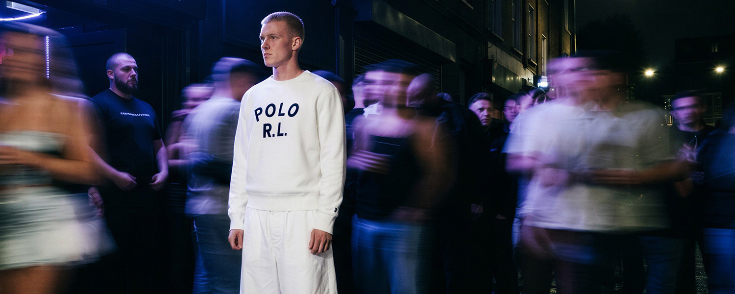Mann in cremefarbenem Sweatshirt mit Logo-Print und weißer Freizeithose in urbaner Abendszene