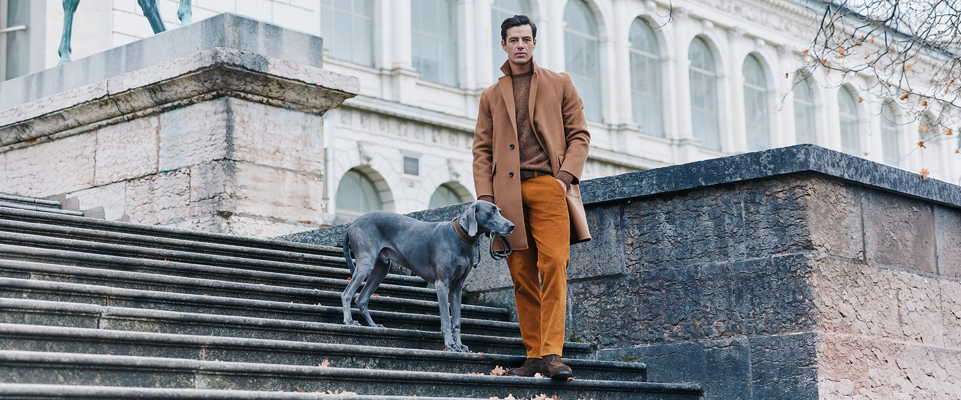 Mann in camelfarbenem Wollmantel und braunem Rollkragenpullover mit ockerfarbener Chino auf Stadttreppe