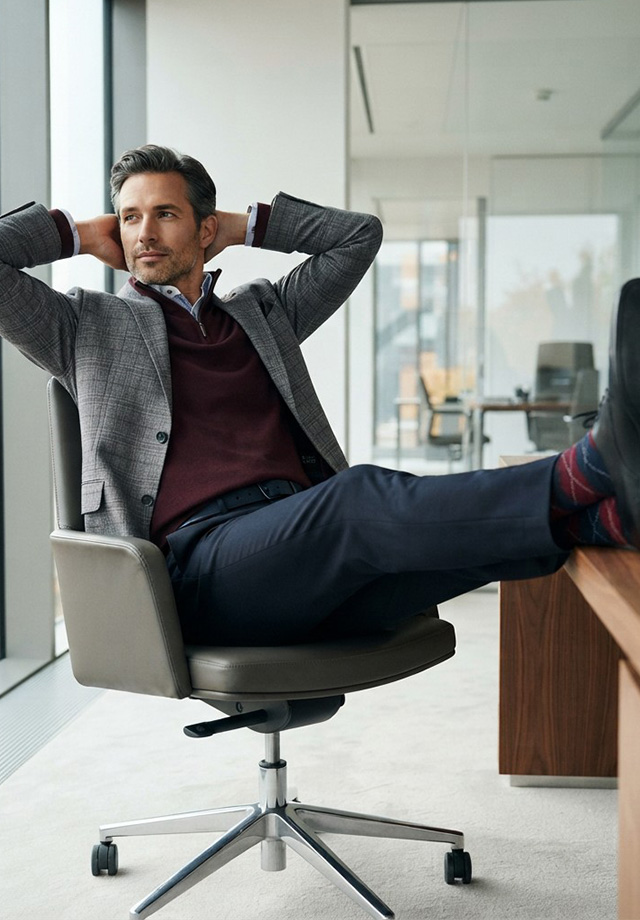 Mann in grauem Sakko mit V-Pullover über hellblauem Hemd, Business-Casual-Look im Büro