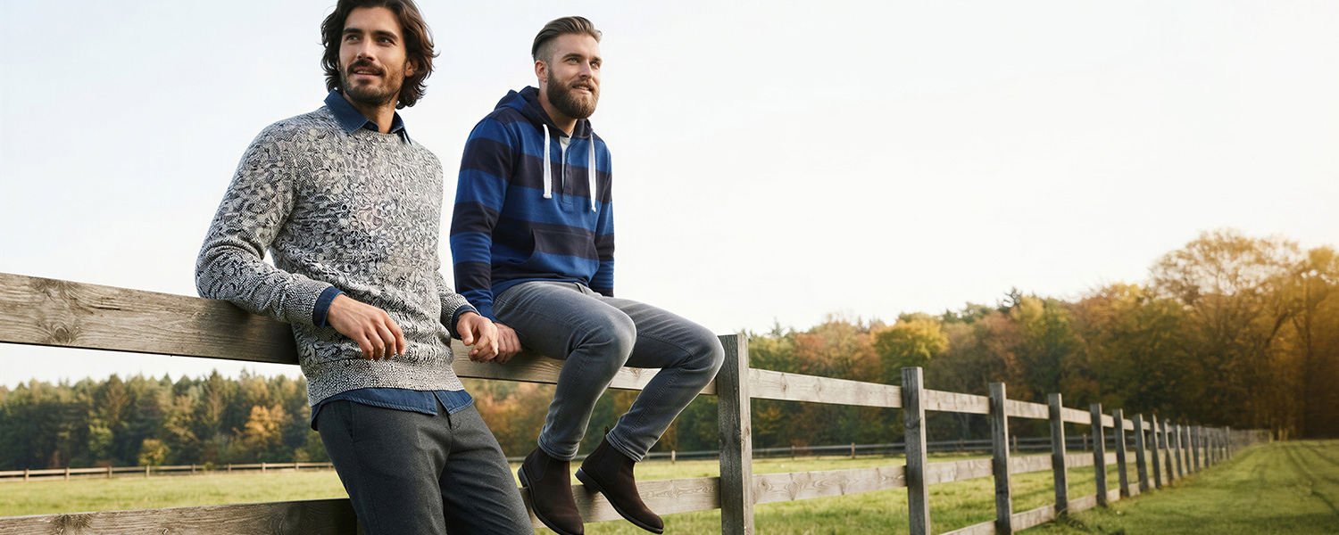 Graumelierter Pullover über blauem Hemd, Mann an Holzzaun im Freien