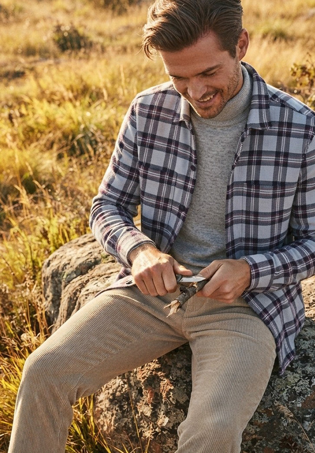 Herren Freizeithemd kariert in Lila-Grau über grauem Pullover, sitzend in der Natur
