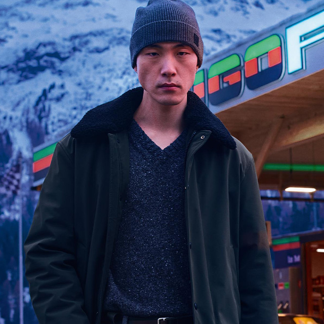 Mann in schwarzem Wintermantel mit Strickpullover und grauer Mütze im Freien