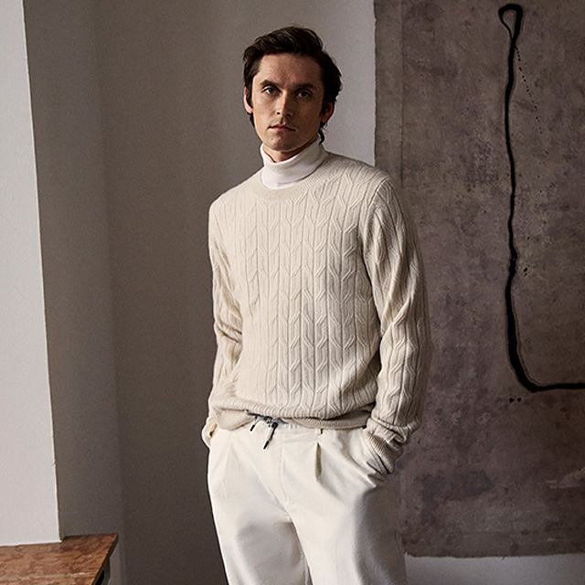 Hellbeiger Strickpullover mit Zopfmuster, über weißem Rollkragenpullover, leger getragen