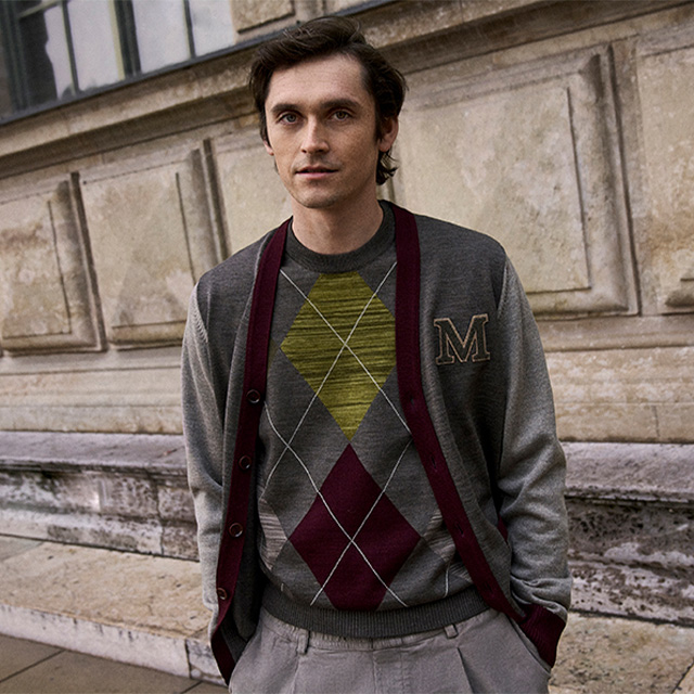 Mann in grauem Argyle-Strickpullover und olivgrüner Cardigan aus Wolle vor Steinwand
