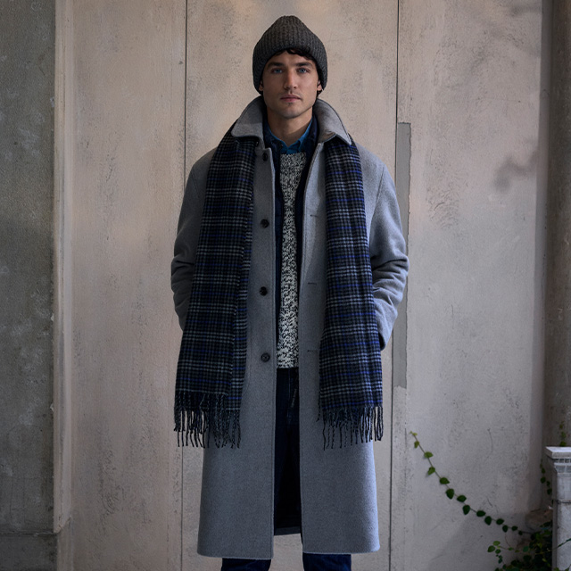 Mann in grauem Wollmantel mit kariertem Schal, getragen mit Strickpulli und Mütze