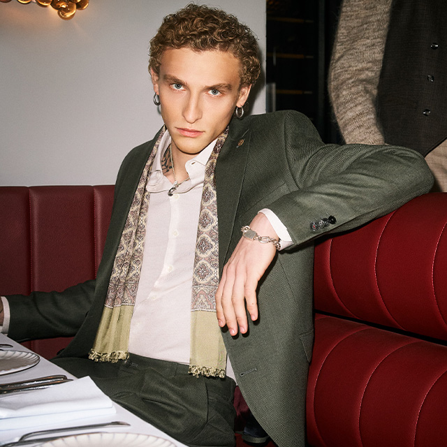 Mann in olivgrünem Anzug mit weißem Hemd, locker sitzend im Restaurant