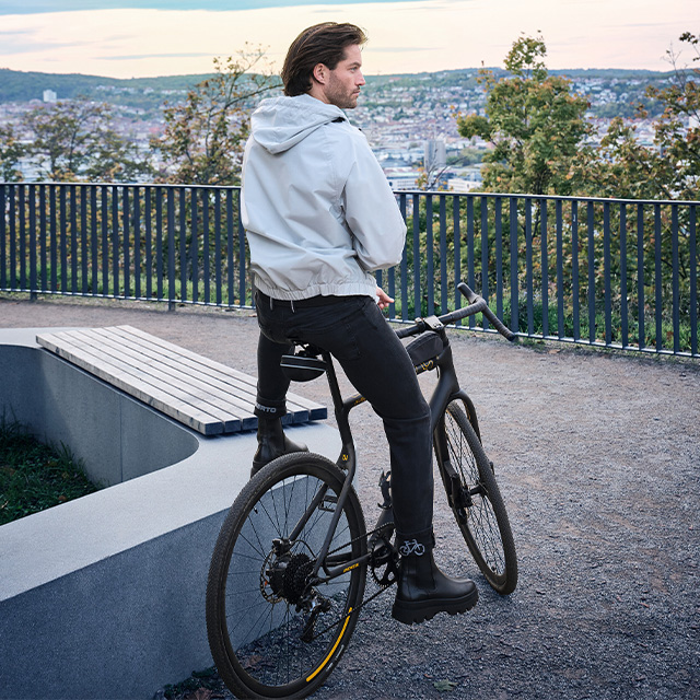 Mann in grauer Jacke und schwarzen Hosen auf einem Fahrrad im Park, seitlich betrachtet
