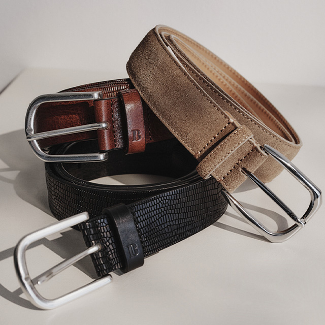 Drei Herrengürtel aus Leder und Wildleder, braun, beige und schwarz, mit silbernen Schnallen.